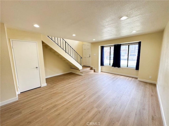 unfurnished living room featuring light wood finished floors, baseboards, stairs, a textured ceiling, and recessed lighting