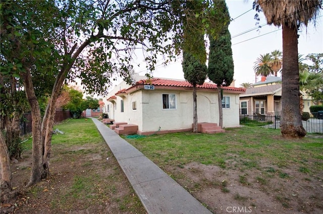 rear view of property featuring a yard, a tile roof, fence, and stucco siding