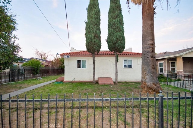 rear view of house featuring fence private yard, a tiled roof, a lawn, and stucco siding