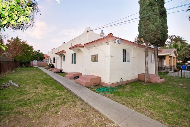 rear view of property featuring a tile roof, fence, a lawn, and stucco siding