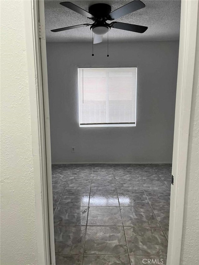 spare room with a textured ceiling, ceiling fan, and baseboards