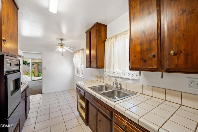 kitchen featuring tile counters, light tile patterned flooring, a sink, ceiling fan, and baseboards