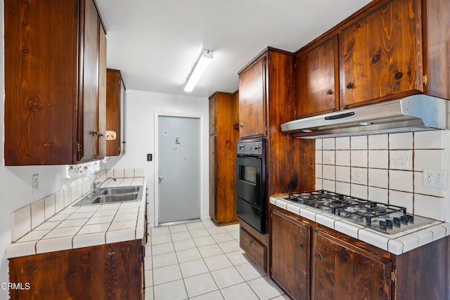 kitchen featuring tile counters, a sink, under cabinet range hood, stainless steel gas stovetop, and backsplash