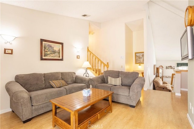 living room with light wood-type flooring, baseboards, stairs, and visible vents