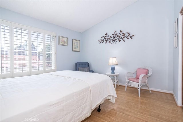 bedroom with vaulted ceiling, wood finished floors, and baseboards