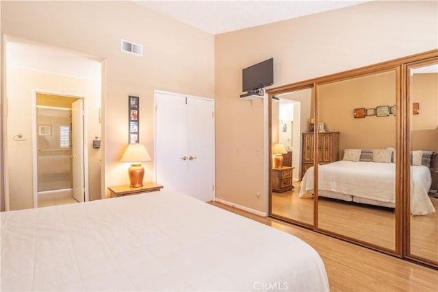 bedroom featuring high vaulted ceiling, a closet, wood finished floors, and visible vents