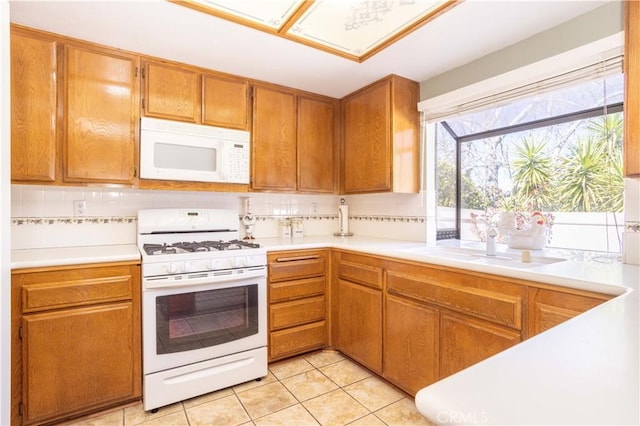 kitchen featuring tasteful backsplash, light countertops, light tile patterned flooring, a sink, and white appliances