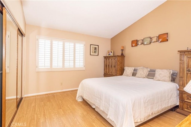 bedroom featuring vaulted ceiling, light wood finished floors, a closet, and baseboards