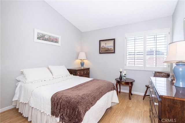 bedroom with baseboards, vaulted ceiling, and light wood finished floors