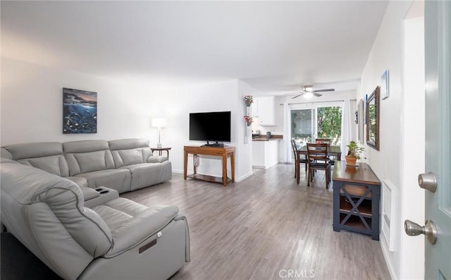 living area featuring light wood finished floors, a ceiling fan, and baseboards