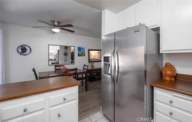 kitchen with stainless steel refrigerator with ice dispenser, light tile patterned floors, dark countertops, white cabinets, and ceiling fan