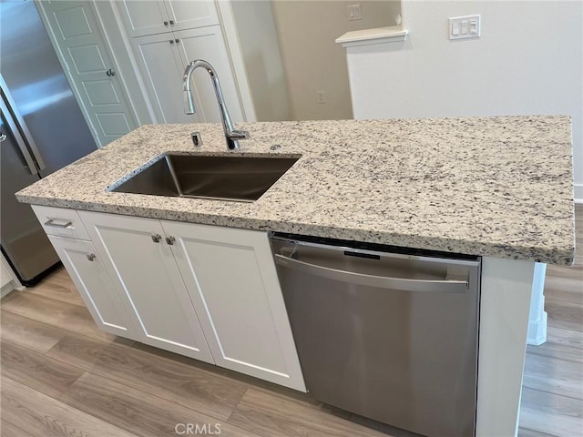 kitchen featuring appliances with stainless steel finishes, white cabinetry, a sink, and light wood finished floors