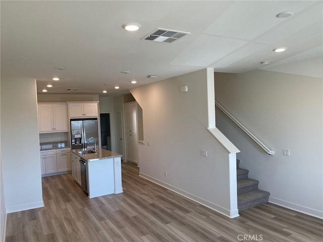 kitchen featuring stainless steel appliances, wood finished floors, a sink, visible vents, and white cabinetry