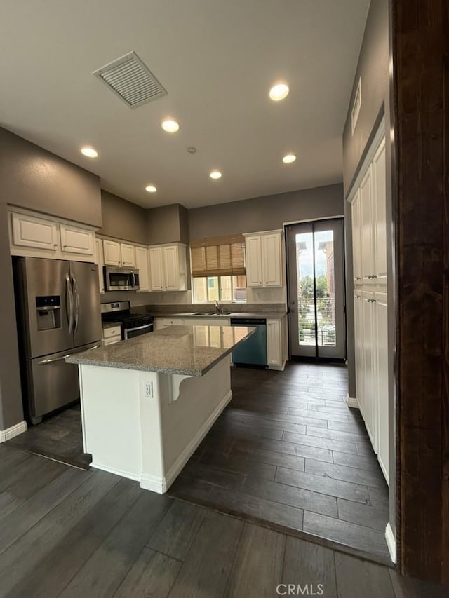 kitchen with visible vents, dark wood-style floors, a center island, stainless steel appliances, and white cabinetry