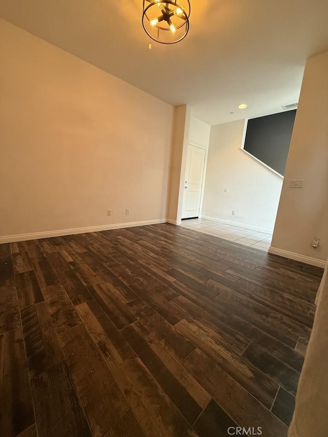 empty room featuring dark wood-style flooring, visible vents, and baseboards