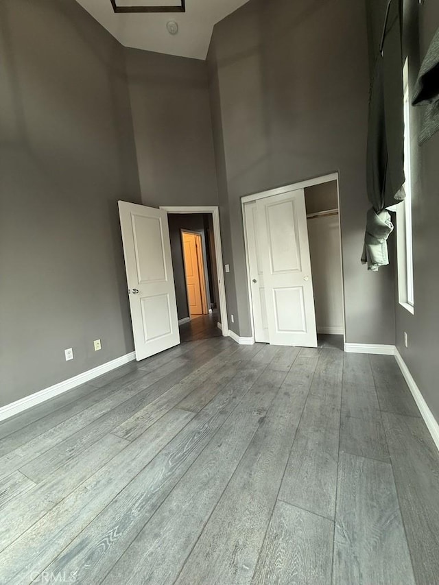 unfurnished bedroom featuring dark wood-style floors, a high ceiling, a closet, and baseboards