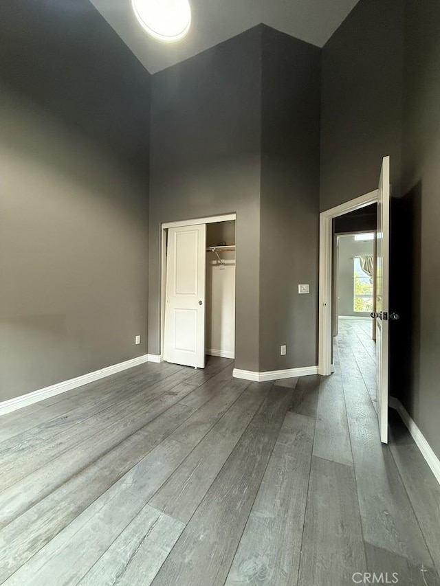 unfurnished bedroom featuring a towering ceiling, a closet, baseboards, and wood finished floors