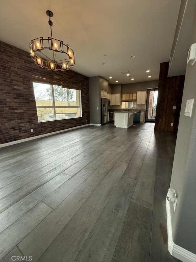 unfurnished living room featuring a chandelier, recessed lighting, dark wood-style flooring, and brick wall