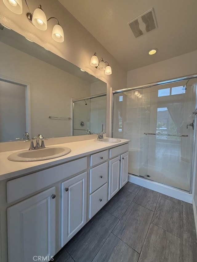 full bath featuring visible vents, a sink, a shower stall, and double vanity