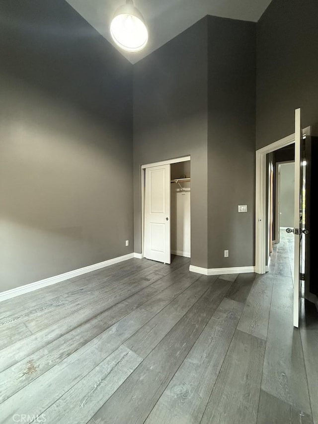 unfurnished bedroom featuring a closet, dark wood-style flooring, a high ceiling, and baseboards