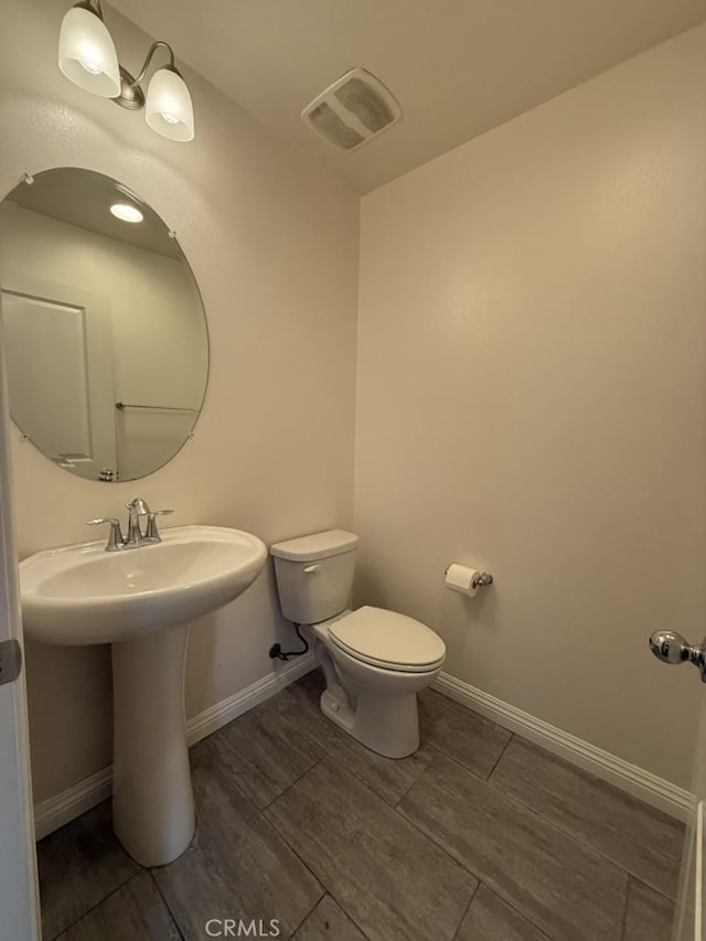 half bath featuring baseboards, visible vents, and toilet