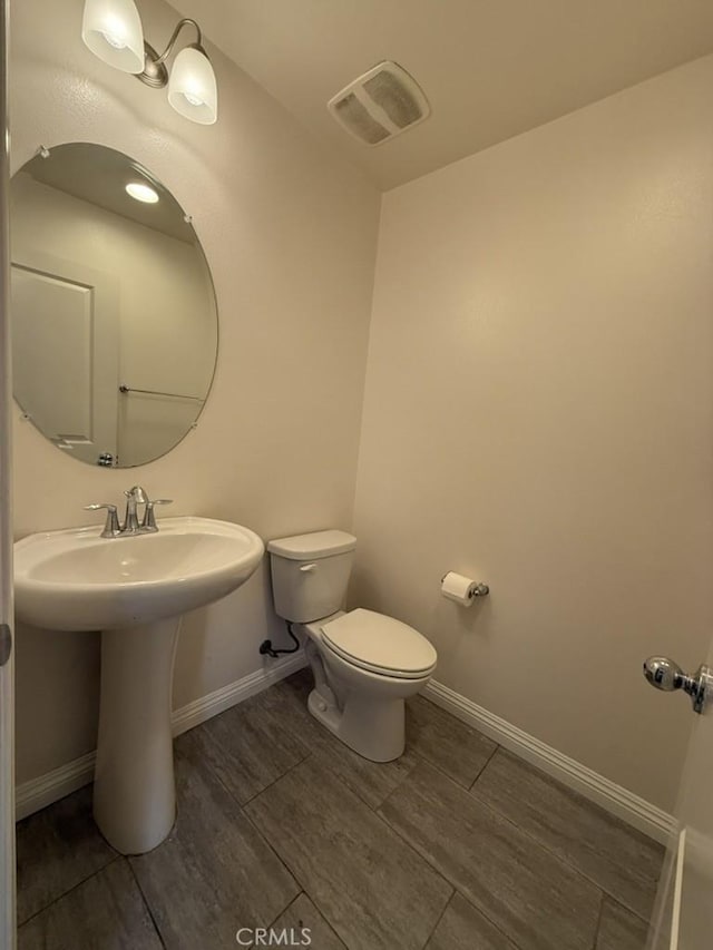 bathroom featuring toilet, a sink, visible vents, and baseboards