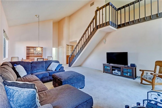 living room featuring carpet flooring, visible vents, a towering ceiling, and stairs