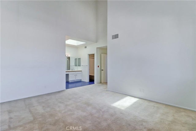 unfurnished living room featuring a towering ceiling, a skylight, carpet flooring, and visible vents