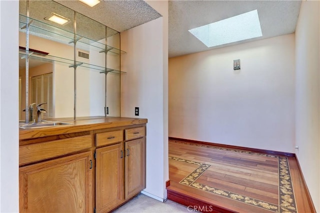 bar featuring a skylight, light wood finished floors, visible vents, a sink, and baseboards