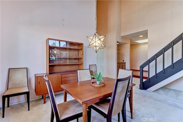 dining area with stairs, baseboards, a towering ceiling, and light colored carpet