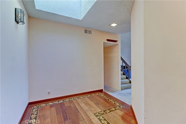 hallway with a skylight, visible vents, baseboards, stairway, and wood finished floors