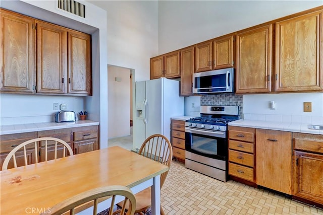 kitchen with tile countertops, stainless steel appliances, a high ceiling, visible vents, and brown cabinets