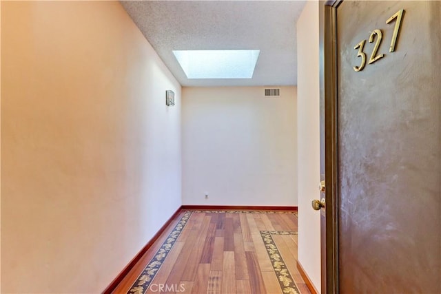 corridor featuring a skylight, wood finished floors, visible vents, and baseboards