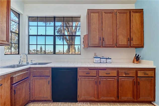 kitchen with black dishwasher, brown cabinetry, a sink, and light countertops