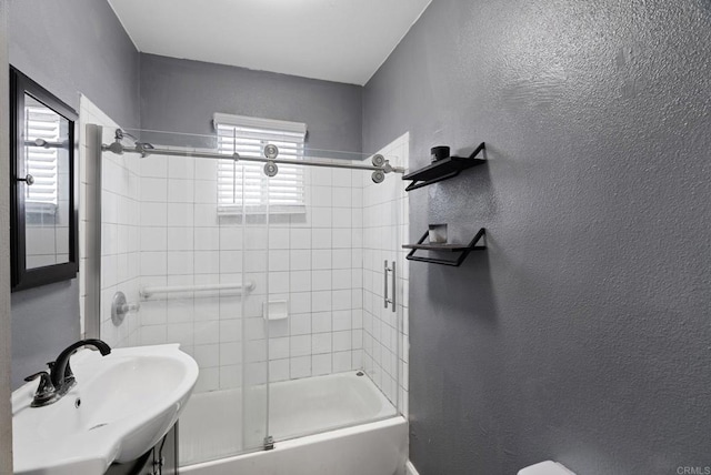 full bathroom with a healthy amount of sunlight, combined bath / shower with glass door, a textured wall, and a sink