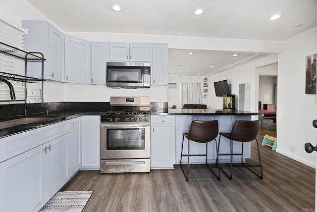 kitchen with a breakfast bar area, dark wood-style floors, a peninsula, a sink, and appliances with stainless steel finishes