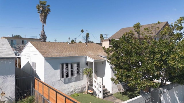 view of front facade featuring entry steps, a fenced backyard, roof with shingles, and stucco siding