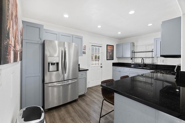 kitchen with dark stone countertops, gray cabinets, dark wood-style flooring, a sink, and stainless steel fridge