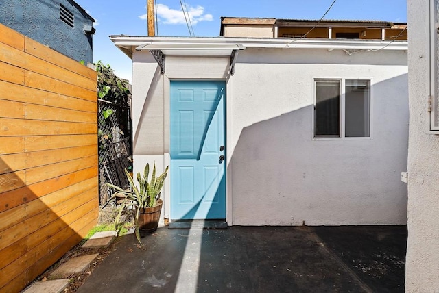 doorway to property featuring stucco siding and fence