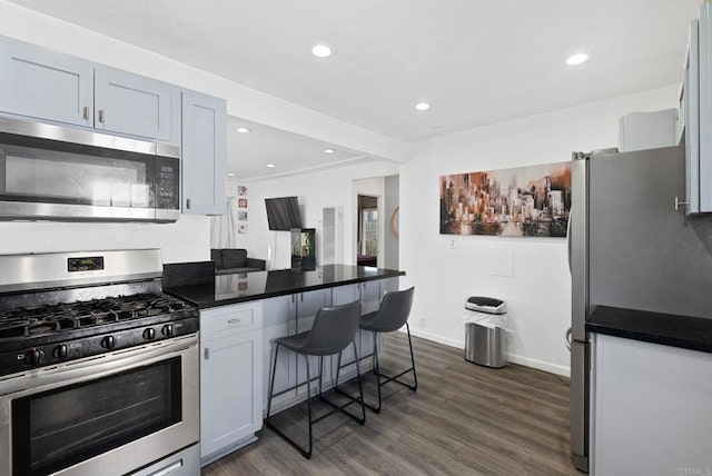 kitchen with a breakfast bar, dark countertops, dark wood finished floors, recessed lighting, and stainless steel appliances