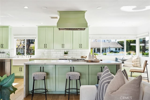 kitchen with green cabinetry, dishwasher, backsplash, and exhaust hood