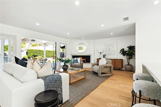 living area with light wood finished floors, recessed lighting, visible vents, and a multi sided fireplace