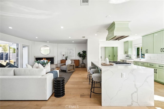 kitchen featuring visible vents, island exhaust hood, a healthy amount of sunlight, a kitchen bar, and green cabinets