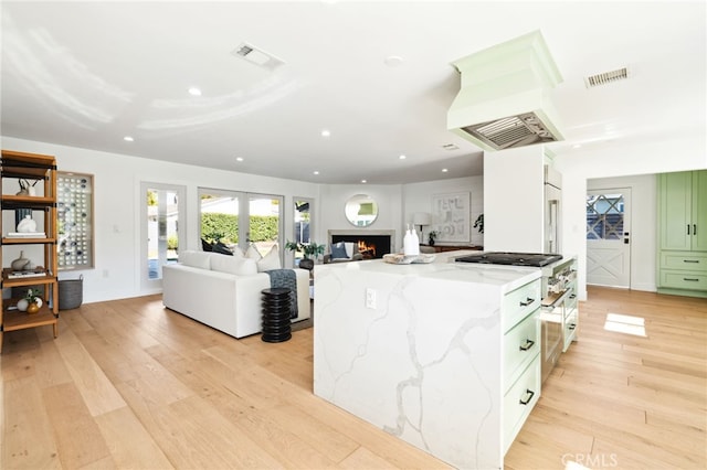 kitchen with a lit fireplace, custom range hood, visible vents, and light wood-style flooring