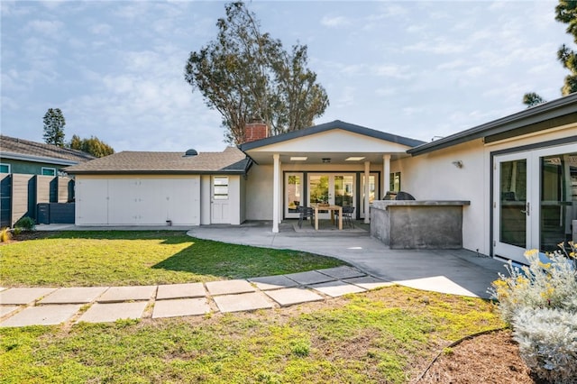 back of house with a chimney, stucco siding, a lawn, a patio area, and exterior kitchen