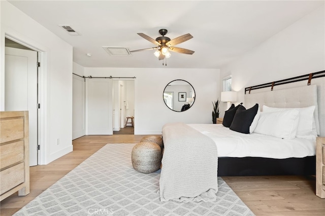 bedroom with light wood finished floors, a barn door, visible vents, baseboards, and a ceiling fan