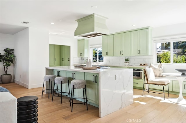 kitchen with tasteful backsplash, green cabinets, light wood-style floors, a kitchen island, and oven