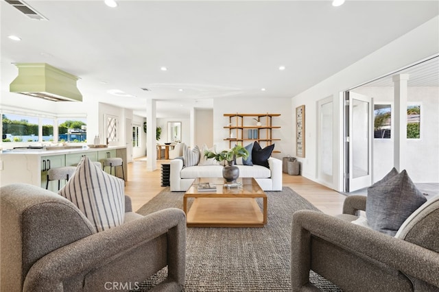 living area with light wood-type flooring, ornate columns, visible vents, and recessed lighting