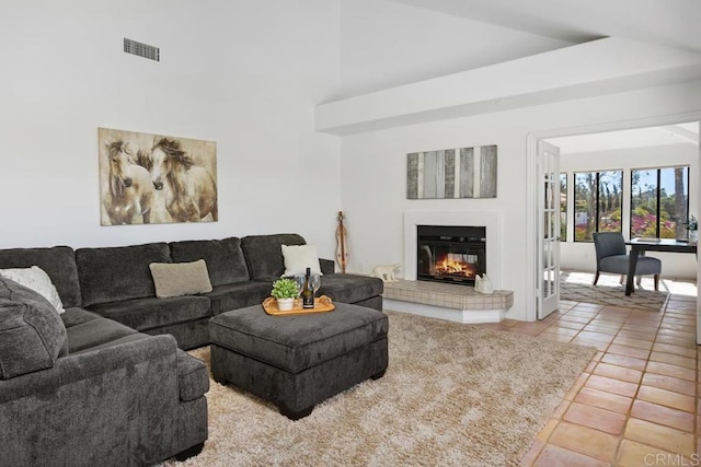 living room with light tile patterned floors, high vaulted ceiling, a glass covered fireplace, and visible vents