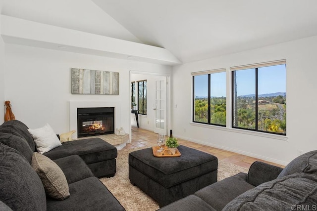 living area featuring lofted ceiling, baseboards, and a glass covered fireplace